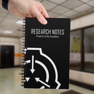Peut inclure: Un carnet à spirales noir avec le texte blanc RESEARCH NOTES et Property of the Foundation en haut, et un grand emblème circulaire blanc contenant trois flèches pointant vers l'intérieur imprimé sur la moitié inférieure de la couverture.