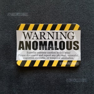 Peut inclure: Un panneau d'avertissement jaune et noir avec le texte "WARNING ANOMALOUS" en noir. Le panneau comprend également le texte "Exercise extreme caution in this area! Please document and report any physical, sensorial, cognitive, memetic, or temporal anomalies." en noir.