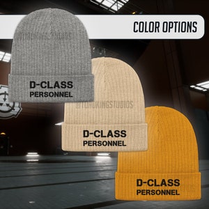 May include: Three knitted beanies in grey, beige, and yellow with the text "D-CLASS PERSONNEL" in black.