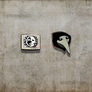 May include: Two enamel pins on a gray background. One pin is a retro television with a pixelated face on the screen. The other pin is a black plague doctor mask with a long beak and blue eyes. The pins are from @TOADKINGSTUDIOS.