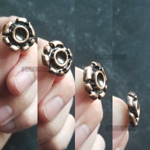 Peut inclure: Gros plan d'une bague en métal de couleur cuivre avec un motif circulaire. La bague a une surface texturée et un centre surélevé.