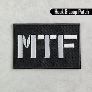 Puede incluir: Un parche rectangular negro con las letras "MTF" bordadas en blanco. El parche tiene un borde negro y el texto "Hook & Loop Patch" en blanco sobre un fondo negro.