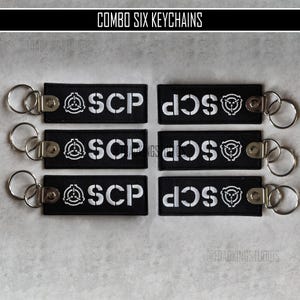 以下が含まれることがあります： 白文字とロゴが入った黒いキーホルダー6個セット。各キーホルダーには「SCP」の文字とシンボルが入っています。キーホルダーにはシルバーのキーリングが付いています。「COMBO SIX KEYCHAINS」の文字が上部にあります。