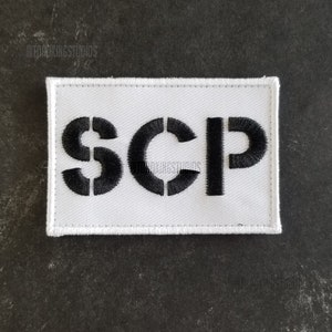 以下が含まれることがあります： 白い布のパッチに黒い刺繍で「SCP」と綴られています。