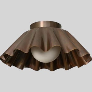 Puede incluir: Una lámpara de techo de color bronce con una pantalla con volantes y festoneada. La pantalla rodea una bombilla esférica blanca. La lámpara tiene una base circular y un diseño vintage.
