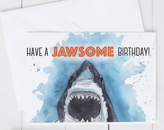 May include: A birthday card with a watercolor illustration of a shark's open mouth. The text on the card reads "Have a Jawsome Birthday!"