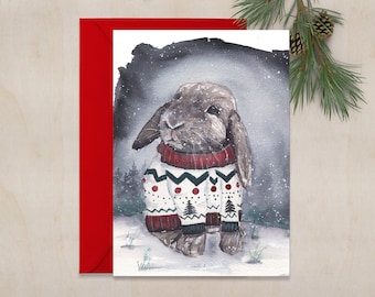 May include: A watercolor painting of a brown rabbit wearing a white and red Christmas sweater with a snowflake pattern. The rabbit is standing in a snowy forest setting.