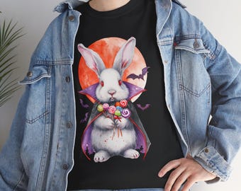 Könnte beinhalten: Schwarzes T-Shirt mit einem Halloween-Motiv. Es zeigt ein weißes Kaninchen im Vampirkostüm, das Lutscher hält, vor einem roten Mond und Fledermäusen. Das Kaninchen hat rote Augen und lange Ohren, mit einem lila Umhang.