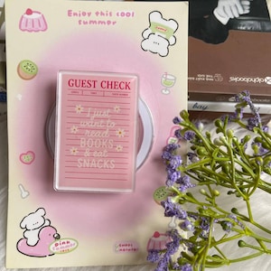 Könnte beinhalten: Ein rosa Gästebon mit dem Text "I just want to read BOOKS & eat SNACKS" wird angezeigt. Der Bon befindet sich auf einem rosa Hintergrund mit Illustrationen zum Thema Sommer. Ein Zweig lila Blumen befindet sich im Vordergrund.
