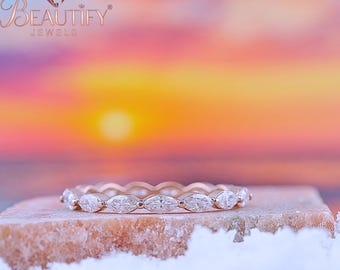 May include: A rose gold eternity ring featuring marquise-cut diamonds. The ring is set on a stone surface with a blurred sunset background. The brand name "BEAUTIFY JEWELS" is visible in the upper left corner.