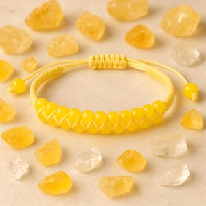 Puede incluir: Una pulsera de cuentas amarillas con cierre de macramé, rodeada de varios cristales amarillos y transparentes. La pulsera presenta una serie de cuentas amarillas, creando una apariencia texturizada. Los cristales varían en tamaño y forma, agregando a la estética natural.