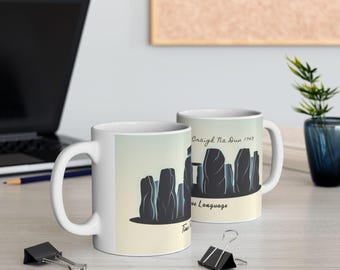 May include: Two white ceramic mugs with a graphic of a stone circle. The design features dark gray silhouettes of standing stones against a light yellow and blue gradient background. Text on the mugs reads "Craigh Na Dun 1743" and "Time is the Language".
