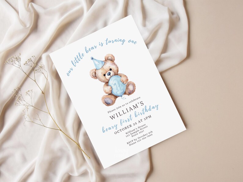 May include: A white invitation card with a watercolor illustration of a teddy bear holding a blue balloon. The text reads "our little bear is turning one" and announces William's first birthday on October 25th at 3 PM.