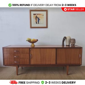 May include: A mid-century modern wooden sideboard with a warm, reddish-brown finish. The cabinet features three drawers on the left, a sliding door in the center, and a door on the right. A framed picture and decorative items sit on top.