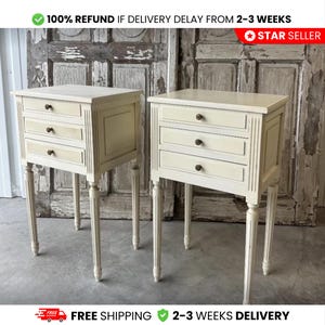 Puede incluir: Dos mesitas de noche color crema, cada una con tres cajones y pomos oscuros. Tienen elegantes patas estriadas y detalles decorativos. La imagen incluye texto que dice "100% REEMBOLSO SI LA ENTREGA SE RETRASA DE 2-3 SEMANAS" y "STAR SELLER".