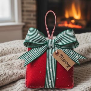 Könnte beinhalten: Roter Weihnachtsbaumschmuck aus Filz in Form einer Geschenkbox, verziert mit einer grün-weiß gestreiften Schleife und Kunstperlen. Ein kleines Etikett mit dem Wort "Merry" hängt an der Schleife. Der Anhänger hat eine rot-weiß gestreifte Aufhängeschlaufe.