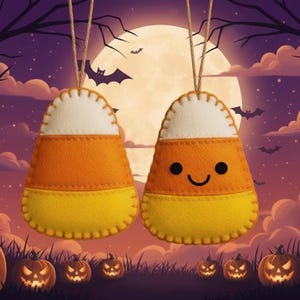 May include: Two felt candy corn ornaments with a white top, orange middle, and yellow bottom, hanging from twine. One has a smiling face. The background features a full moon, bats, and jack-o'-lanterns, creating a Halloween theme.