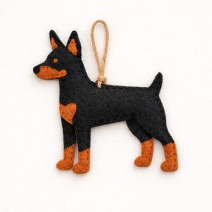 May include: A handmade felt dog ornament in black and brown. The dog has a heart-shaped patch on its side and a jute string for hanging. The dog's ears, snout, and legs are brown.