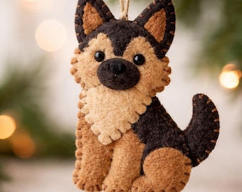 May include: A felt ornament shaped like a German Shepherd dog. The dog has a tan body with black and brown markings, black eyes, and a black nose. A twine loop is attached for hanging. The ornament is likely for Christmas.
