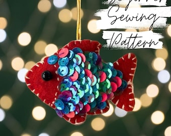 May include: A red felt fish ornament featuring iridescent blue and green sequins, a black bead eye, and white whip-stitched edges. The fish hangs from a gold cord and includes the text Beginner Sewing Pattern in white script on a textured background.