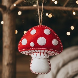 May include: A red and white felt mushroom ornament with white polka dots and a white stem. The ornament is hanging from a natural twine string. The mushroom is a festive decoration for the holiday season.