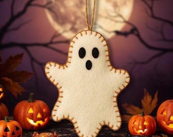May include: A felt ghost ornament with black eyes and mouth, stitched with brown thread, hangs against a Halloween backdrop. Lit jack-o'-lanterns, candy corn, and autumn leaves complete the spooky scene.
