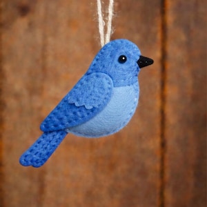 Puede incluir: Adorno de pájaro azul hecho a mano con fieltro, suspendido por una cuerda de hilo natural. El pájaro presenta un cuerpo azul claro, alas y cola azul oscuro, un pico negro y un pequeño ojo negro. Ideal para decorar.