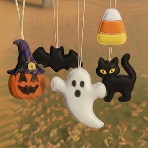 May include: A collection of Halloween-themed felt ornaments. Includes a jack-o'-lantern with a witch's hat, a black bat, a white ghost, a black cat with yellow eyes, and a candy corn. Each ornament is suspended by a string.