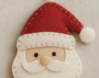 May include: A handmade Christmas ornament shaped like Santa Claus's face. The ornament is made of red and white felt, with a white beard, mustache, and hat trim. It has black eyes, a small pink nose, and a white string for hanging.