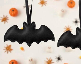 May include: Black bat-shaped Halloween ornaments with stitched edges hang from black ribbons. The background features small orange pumpkins, star-shaped decorations, and ghost-shaped candies, creating a festive holiday scene.