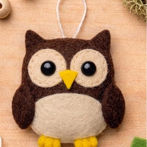 May include: A handcrafted felt owl ornament. The owl features a brown body, large black eyes, and a yellow beak. The owl has a cream-colored chest and eye surrounds. A white string is attached for hanging. The owl's feet are yellow.