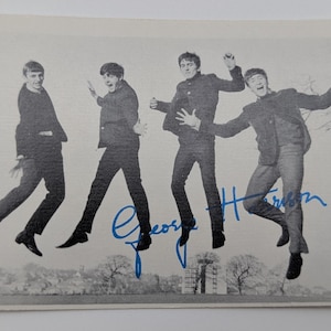 Może przedstawiać: Czarno-białe zdjęcie The Beatles skaczących w powietrzu. Zdjęcie jest podpisane niebieskim atramentem przez George'a Harrisona. Członkowie zespołu mają na sobie ciemne garnitury i czarne buty. W tle widoczny jest krajobraz.