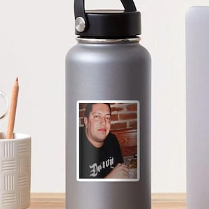 May include: A sticker featuring a photograph of a person wearing a black t-shirt with the word "Detroit" in a stylized font. The background is a brick wall.