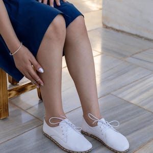 Op de afbeelding: Een paar witte leren oxford-schoenen met een ronde neus, dunne witte veters en zichtbare stiksels langs de rand van de zool. De schoenen hebben een laag profiel met een gladde afwerking en een strakke, eenvoudige constructie voor dagelijks gebruik.