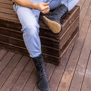 May include: Black leather lace-up boots with a side zipper. The boots have a natural-colored sole and are worn with blue jeans. The boots are mid-calf height and have a classic, rugged design.
