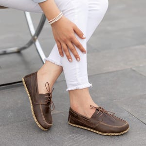 May include: Brown leather boat shoes with a classic design. The shoes feature a lace-up closure and a stitched sole. The leather has a rich, dark brown color, and the soles have a natural, light brown hue. These shoes are a stylish footwear option.