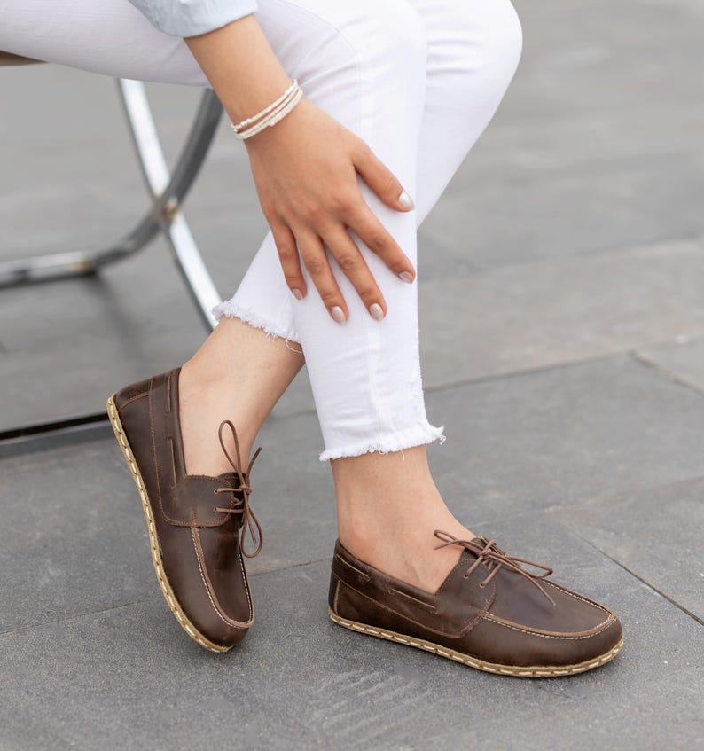 May include: Brown leather boat shoes with a classic design. The shoes feature a lace-up closure and a stitched sole. The leather has a rich, dark brown color, and the soles have a natural, light brown hue. These shoes are a stylish footwear option.