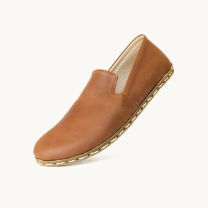 May include: A single brown leather slip-on shoe. The shoe has a rounded toe and a low profile. The sole is stitched with a light-colored thread. The shoe is made of a smooth, polished leather.