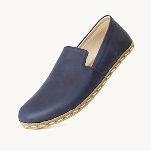 May include: A single navy blue leather slip-on shoe. The shoe has a rounded toe and a low profile. The sole is a light brown color with white stitching around the edge. The interior of the shoe is a light beige color.