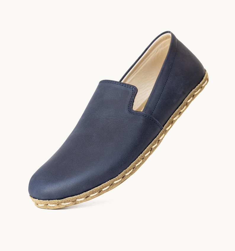 May include: A single navy blue leather slip-on shoe. The shoe has a rounded toe and a low profile. The sole is a light brown color with white stitching around the edge. The interior of the shoe is a light beige color.