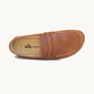 May include: A single brown leather loafer shoe with white stitching and a strap across the top. The shoe has the text "ede BAREFOOT SHOES" printed on the insole. The shoe is a size W6.
