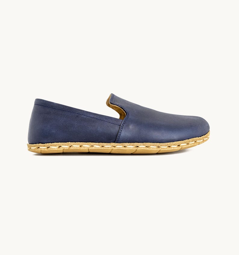 May include: A single blue leather slip-on shoe with a natural-colored sole. The shoe has a rounded toe and a low profile, with visible stitching around the sole. The leather appears to have a slightly distressed finish.