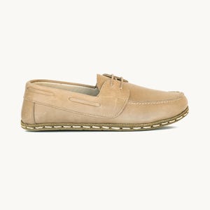 Könnte beinhalten: Ein hellbrauner Lederschuh im Mokassin-Stil mit flacher Silhouette und einer dicken, sichtbaren weißen Steppnaht entlang der Sohle. Der Schuh verfügt über eine kleine Schnürung auf der Oberseite und eine glatte, matte Oberfläche.