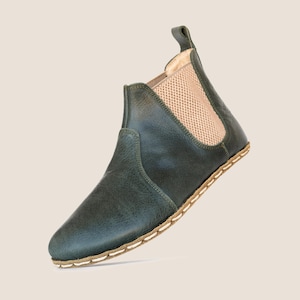 Op de afbeelding: Donkergroene leren Chelsea boot met een beige mesh paneel en een treklipje. De zool is gestikt met witte draad. Een stijlvol, minimalistisch ontwerp voor dagelijks gebruik.