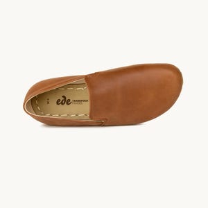 May include: A single brown leather slip-on shoe with a rounded toe. The shoe has a stitched sole and the brand name "ede BAREFOOT SHOES" is visible. The shoe is a size W6.