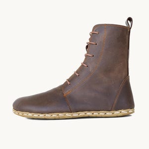 Puede incluir: Bota de cuero marrón con diseño de cordones. La bota presenta una puntera redondeada, una suela cosida y una presilla en la parte superior. El cuero tiene un aspecto envejecido y los cordones son de color marrón claro.