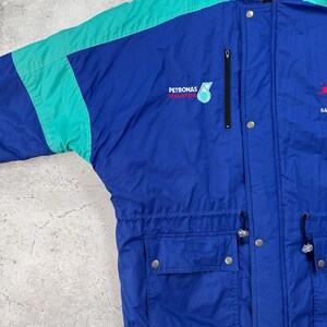 Pu&ograve; includere: Giacca vintage blu e turchese con il logo "PETRONAS MALAYSIA". La giacca ha un cappuccio, una cerniera e pi&ugrave; tasche. Le maniche sono turchesi e il corpo blu. Ha una vita regolabile e chiusure a scatto.
