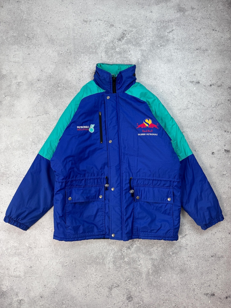 Pu&ograve; includere: Giacca blu, verde acqua e blu navy con la scritta "PETRONAS MALAYSIA" e "SAUBER PETRONAS". La giacca ha un collo alto, una cerniera e pi&ugrave; tasche. La giacca &egrave; in stile vintage.