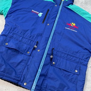 Pu&ograve; includere: Giacca vintage blu e verde acqua con i loghi Petronas e Red Bull Sauber Petronas. La giacca ha una chiusura a zip, due tasche frontali e una vita con coulisse. Un metro a nastro &egrave; appoggiato sulla giacca.