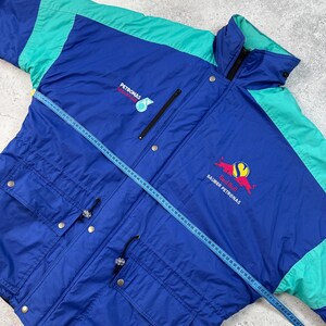 Pu&ograve; includere: Giacca vintage blu e verde acqua con i loghi Petronas e Red Bull Sauber Petronas. La giacca ha una chiusura a zip, tasche multiple e un cordoncino in vita. Un metro a nastro &egrave; appoggiato sulla giacca.